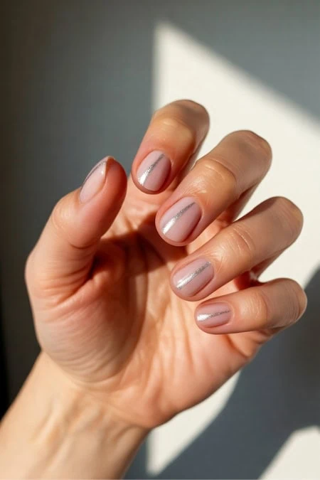 Close-up of a hand with neatly manicured nails featuring a subtle nude polish and delicate silver line accents, illuminated by natural sunlight.