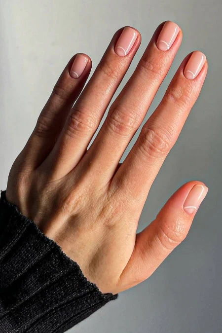 Close-up of a hand with well-manicured, natural-looking nails against a neutral background, showcasing healthy and polished nails.
