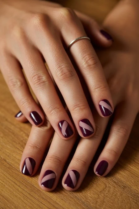 Elegant manicured nails with geometric purple and nude nail art on well-groomed hands resting on a wooden surface.