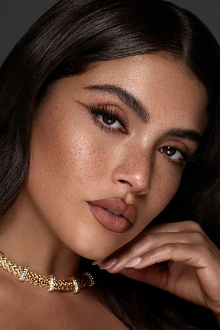 Close-up of a woman with flawless skin, brown eyes, long eyelashes, and dark hair, showcasing natural beauty and fall makeup looks.