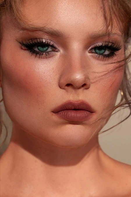 Close-up of a woman with bold fall makeup featuring smoky eyes, defined eyebrows, and matte nude lips, perfect for autumn beauty looks.