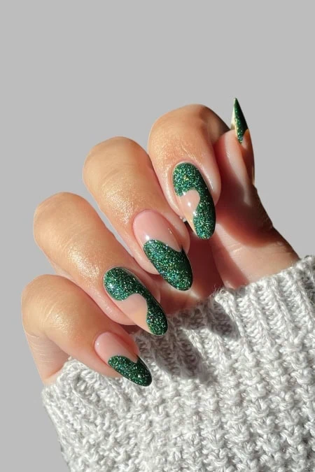 Gorgeous green glitter nail art on long almond-shaped nails, perfect for all year round, with a cozy gray sweater in the background.