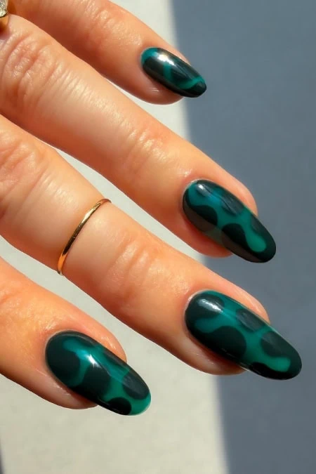 Gorgeous green nails with a glossy finish and black polka dot design, perfect for all year round, showcased on a hand with a gold ring.