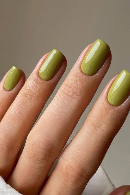 Close-up of a hand with neatly manicured nails painted in a vibrant green color, showcasing a trendy nail art style.