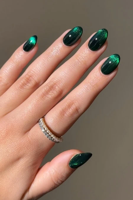 Gorgeous green nail design with a shimmering finish on almond-shaped nails, perfect for all year round. Featuring a stylish ring on the finger.