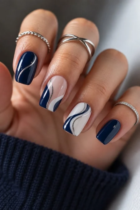 Elegant navy blue and white marbled nail art on manicured fingers with silver rings, showcasing stylish and modern nail design.