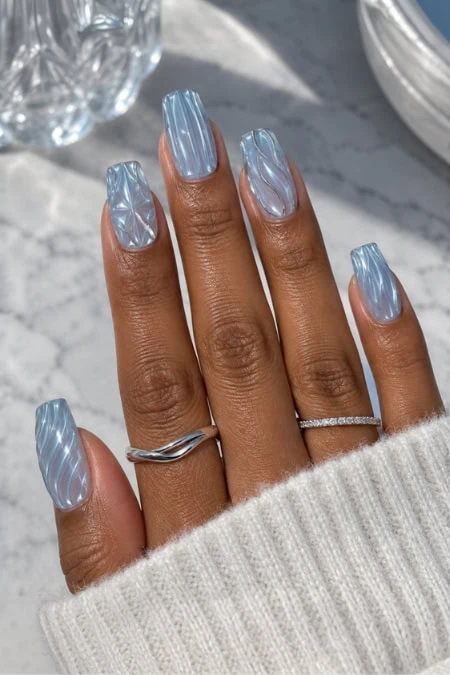 Elegant manicure featuring iridescent, holographic nail polish with a wavy pattern, showcased on a hand with rings and a cozy sweater sleeve.