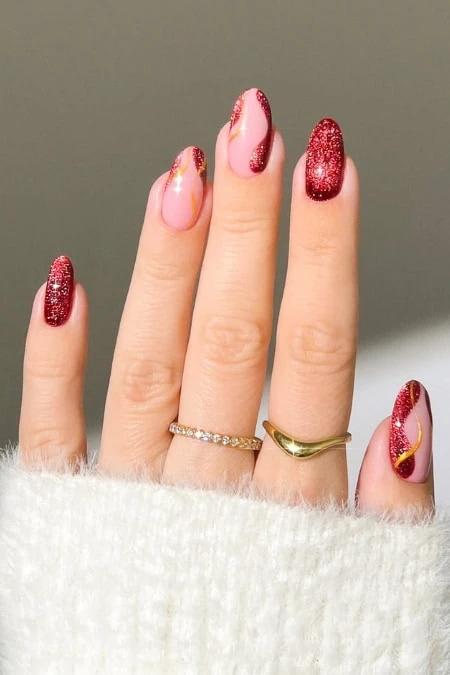 Elegant manicure featuring pink and red glitter nail polish on a woman's hand with gold rings, showcasing festive and stylish nail art.