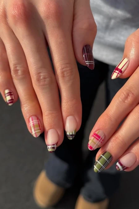 Colorful plaid nail art with red, green, and beige tones on well-manicured nails, perfect for fall or holiday fashion.