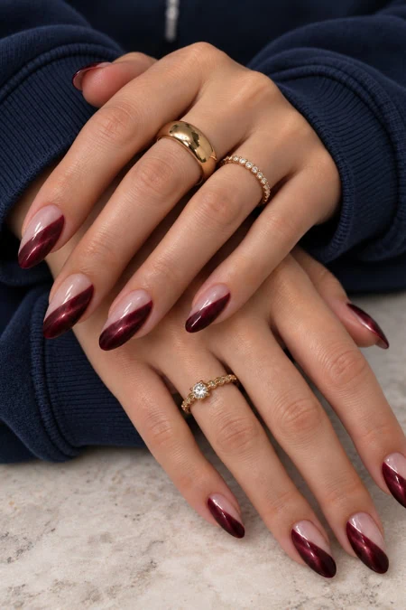 Close-up of a woman's hands with manicured nails and multiple rings, wearing a dark blue sweater, on a light surface.