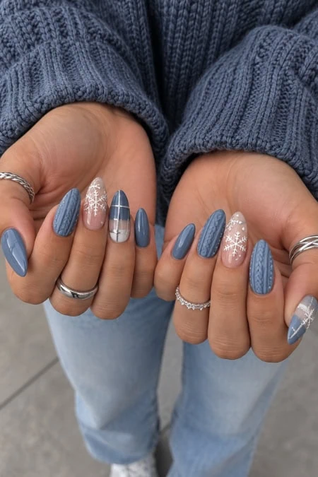 Close-up of hands with stylish blue and white winter-themed nail art, featuring snowflake designs and plaid accents, wearing cozy gray sweaters.