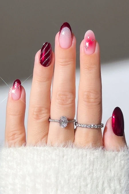 Elegant manicured nails with red and pink gradient polish, accented with glitter and small rhinestones, showcasing stylish nail art and a diamond ring on the middle finger.