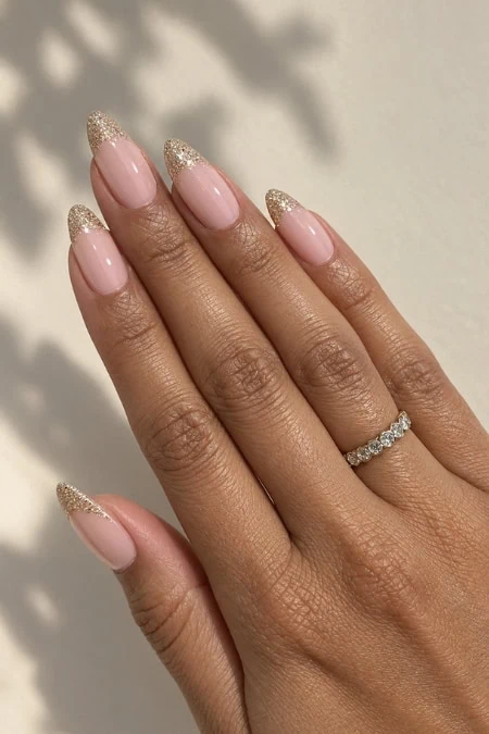 Elegant manicure with nude pink nails and gold glitter tips, featuring a diamond ring on the ring finger, perfect for beauty and jewelry enthusiasts. Perfect look for winter nail designs.