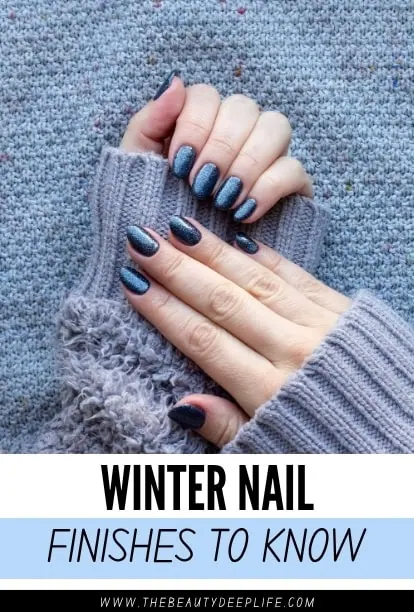 Close-up of hands with winter-themed dark blue and glittery nail polish, wearing cozy gray knit sweater, on a textured background.