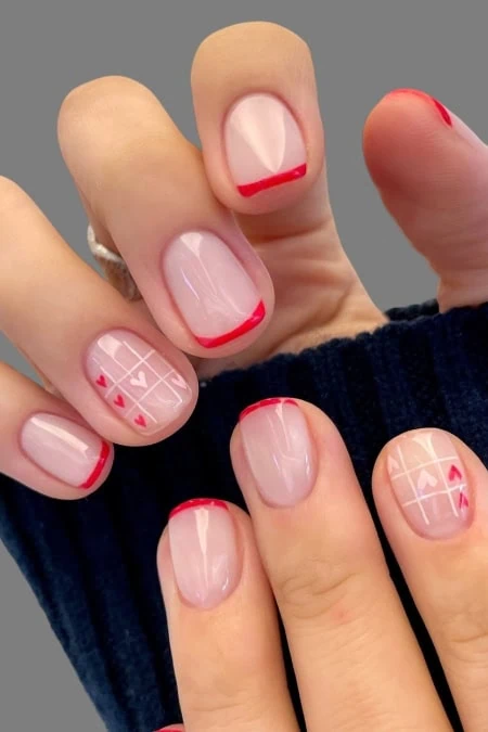 Manicure with pale pink nails and red French tips, geometric accent nails on ring fingers, close-up of stylish nail design suitable for beauty and nail care SEO.