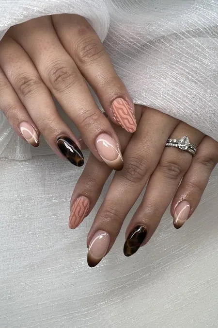 Stylish almond nails with nude gradient and tortoiseshell accents, featuring delicate white vine pattern on the ring finger and a statement ring, perfect for a chic salon look.