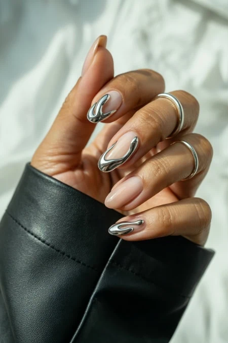 Close-up of a hand with glossy almond-shaped winter nails trend featuring a silver and gray marble nail art design, wearing multiple silver rings against a soft light background.