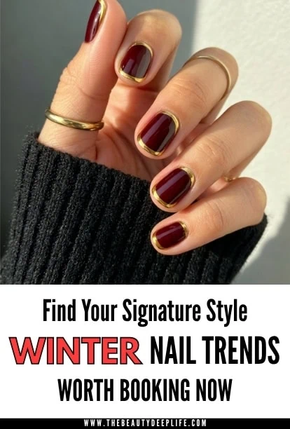 Close-up of nails with dark burgundy polish and gold metallic tips, stylish winter manicure, cozy black sleeve framing the hand.